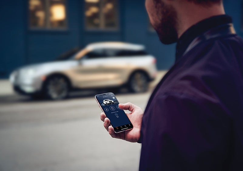 A person is shown interacting with a smartphone to connect to a Lincoln vehicle across the street. | Palmetto Lincoln in Charleston SC