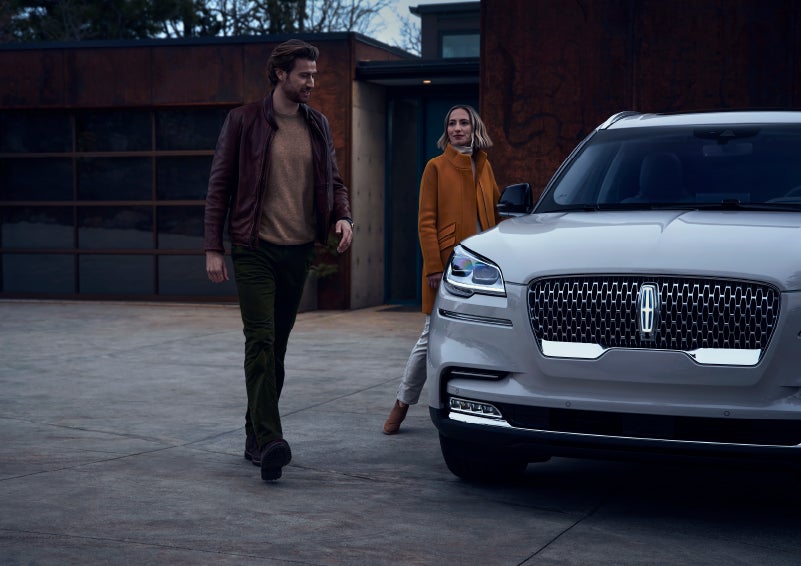 A man and a woman approaching a 2024 Lincoln Aviator® SUV, which illuminates certain lights when they are close | Palmetto Lincoln in Charleston SC